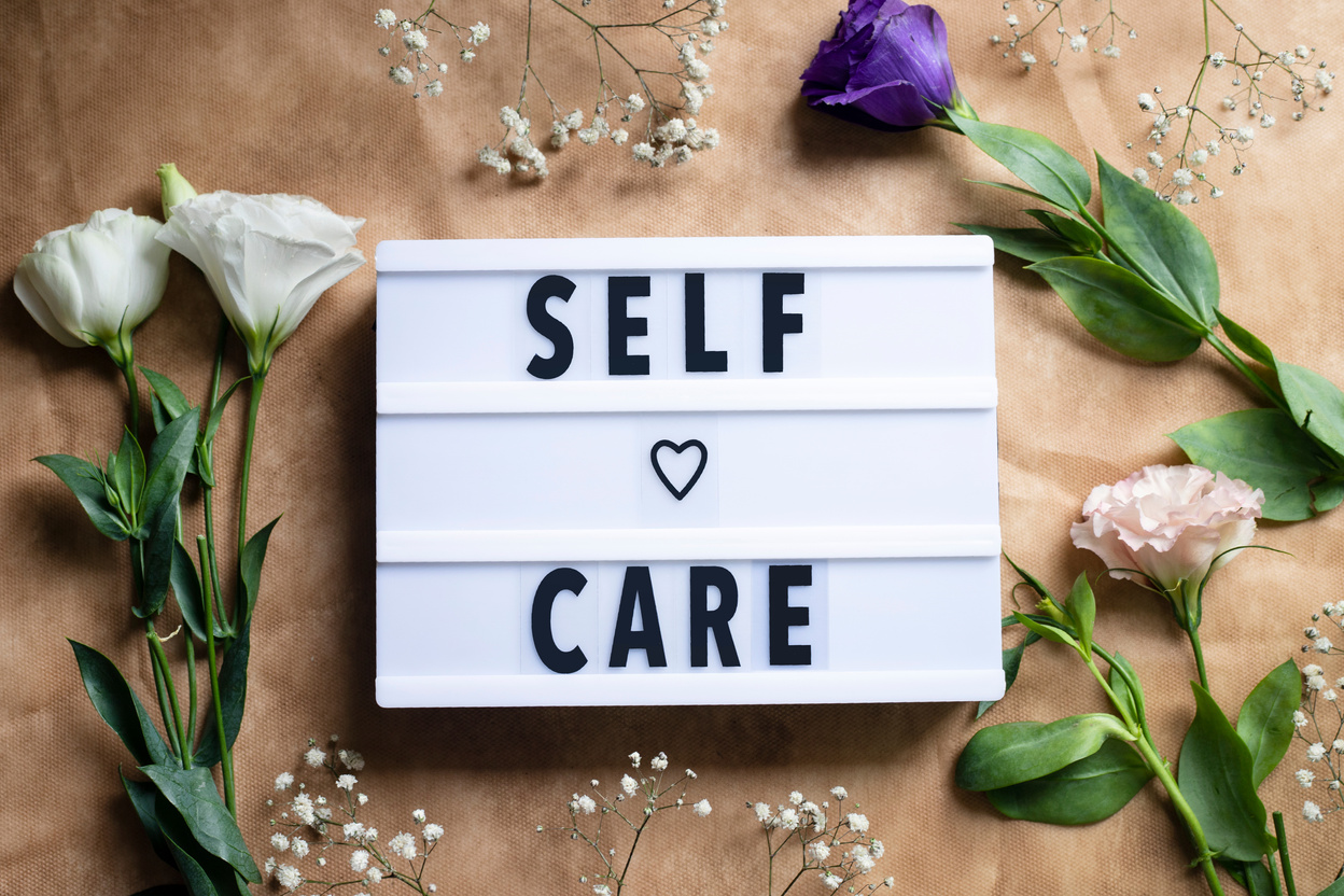 Self-care word on lightbox and flowers on color background flat lay. Take care of yourself
